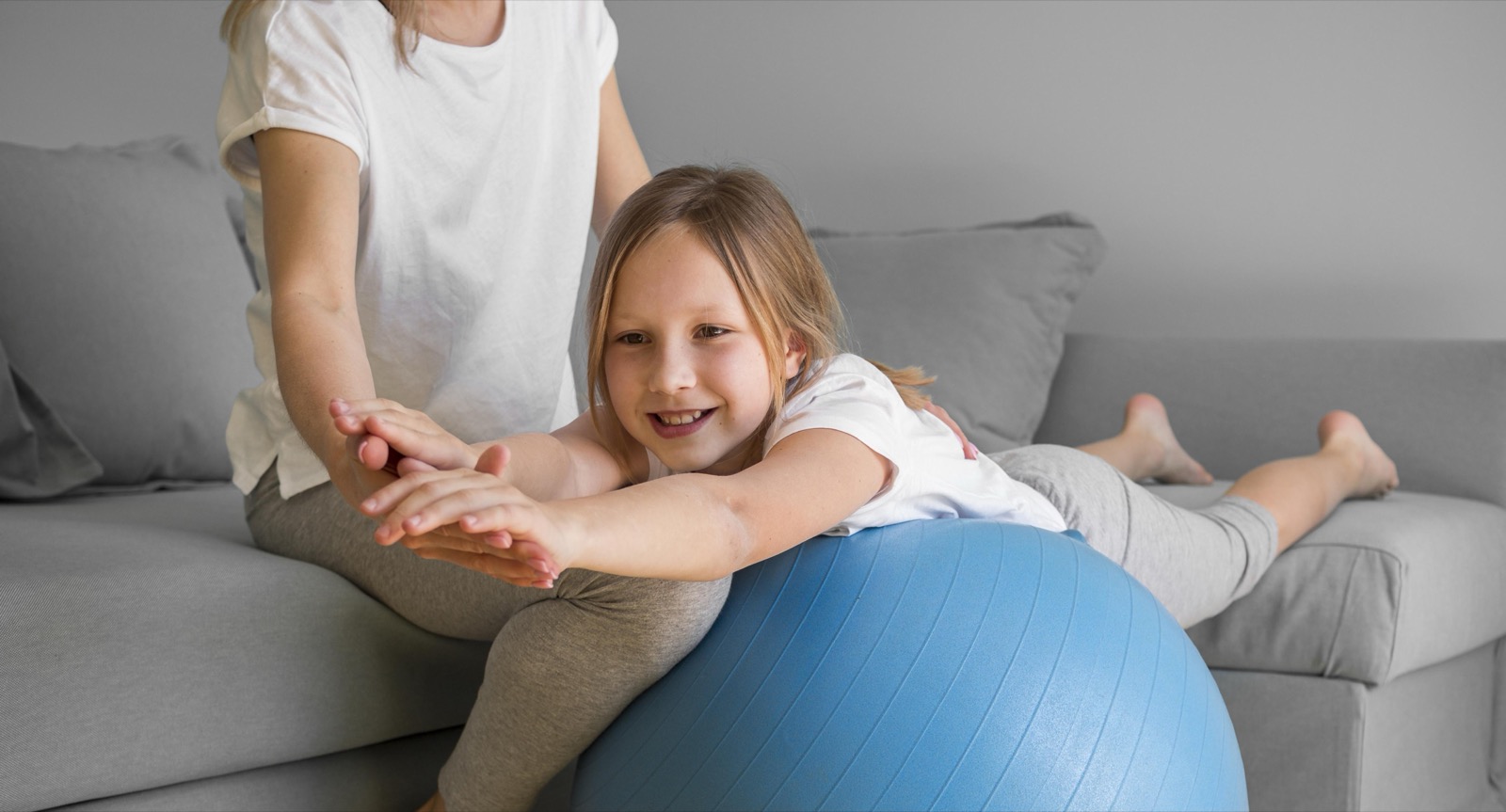 A mother helping her daughter exercise on a therapy ball