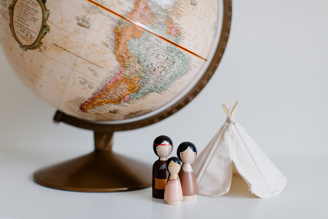 Free From above of miniature toys tipi house and American Indian family placed near vintage globe against gray background at daytime Stock Photo
