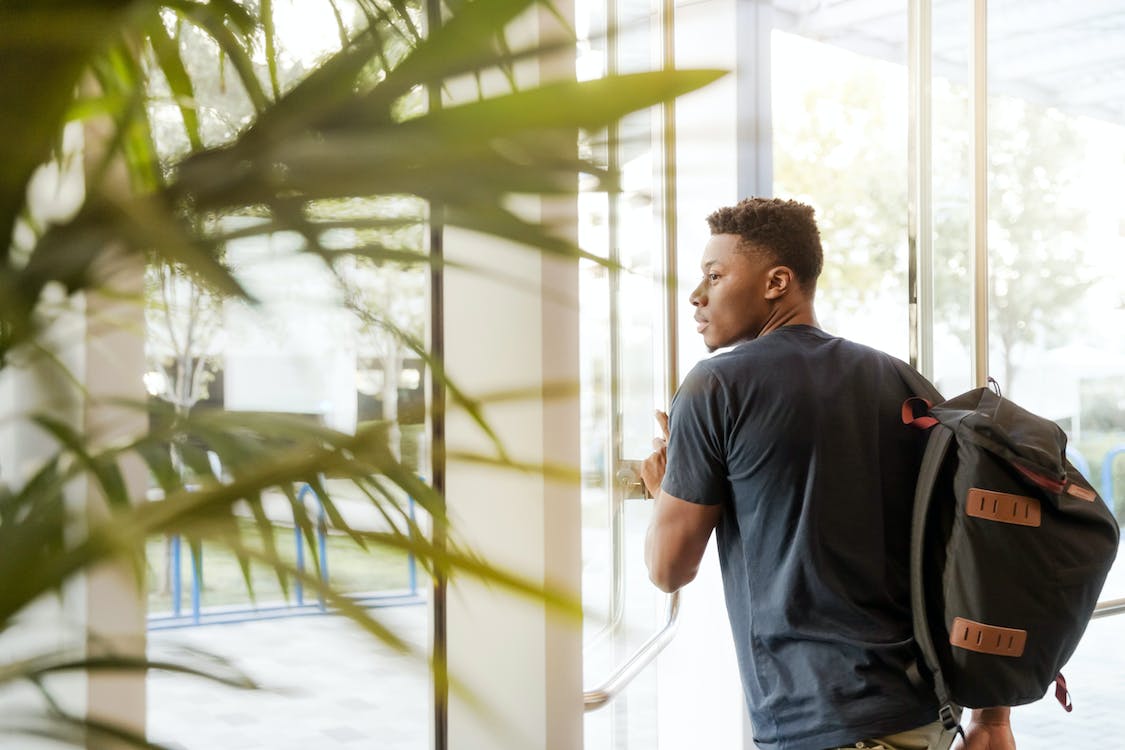 Free Man Looking Outside Window Carrying Black and Brown Backpack While Holding His Hand on Window Stock Photo