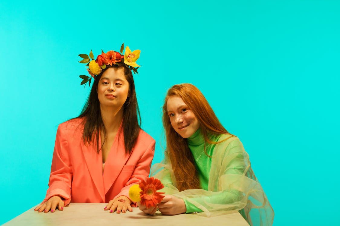 Free Women in Stylish Outfits Posing with Flowers while Sitting at a Table Stock Photo