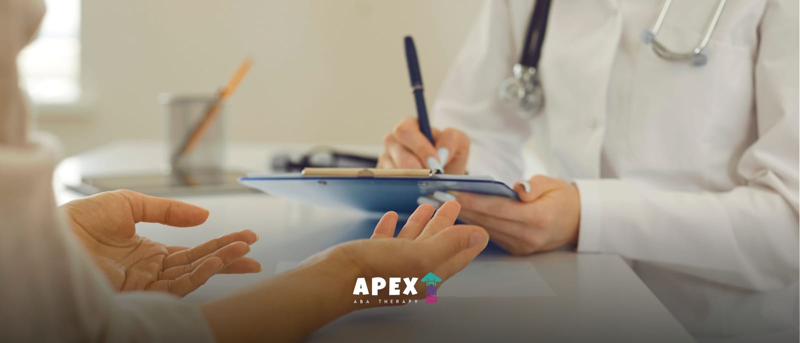 Doctor in a white coat writing on a clipboard while a patient gestures across the desk during a consultation.
