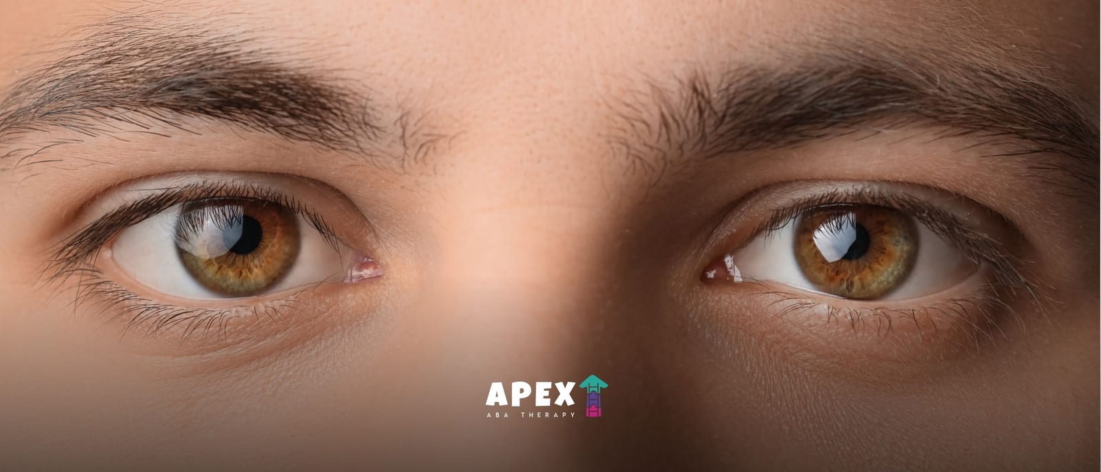 Close-up of a person’s hazel eyes and dark eyebrows looking directly at the camera, with soft lighting and a calm, focused expression.