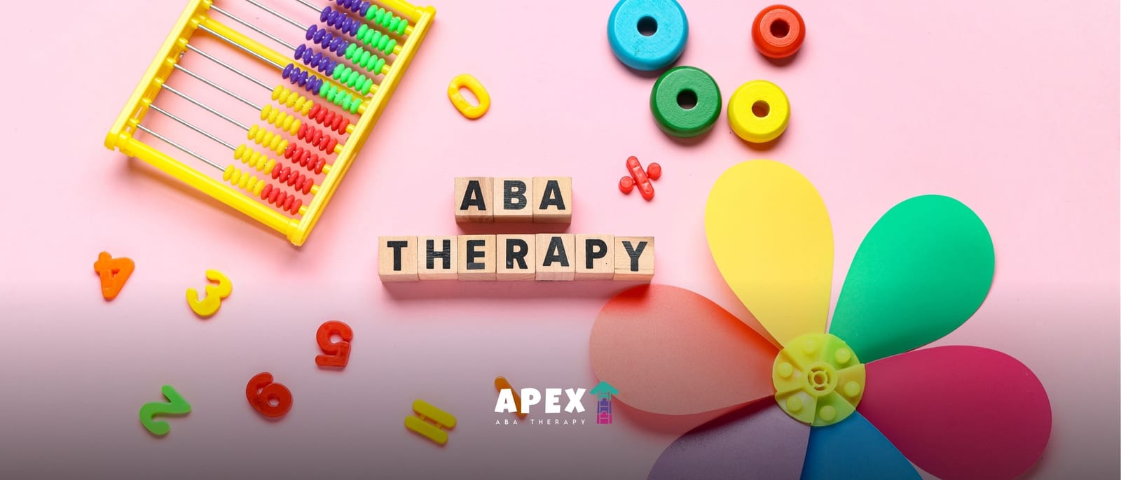Wooden blocks spelling ABA THERAPY on a pink background with a colorful abacus, plastic numbers, stacking rings, and a multi-colored toy pinwheel.