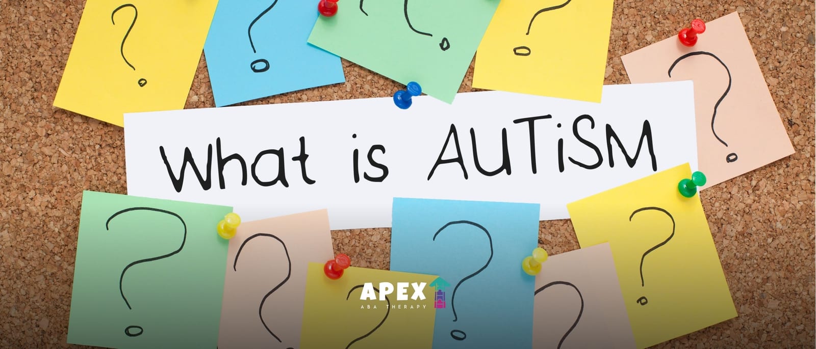 A colorful autism awareness poster on a corkboard reads “What is autism?” amid question-mark notes.
